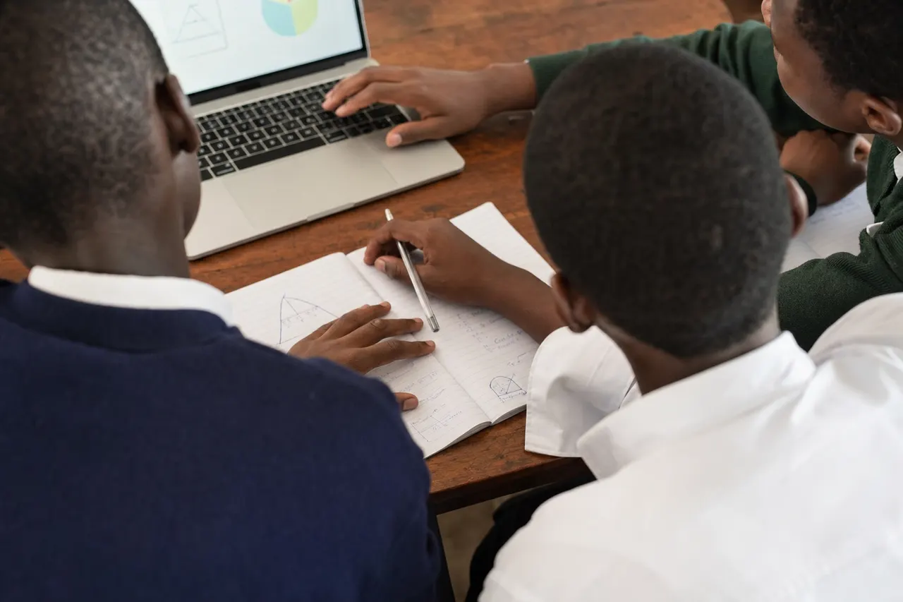 Illustrative over-the-shoulder view of Tanzanian students collaborating with notebooks and a computer